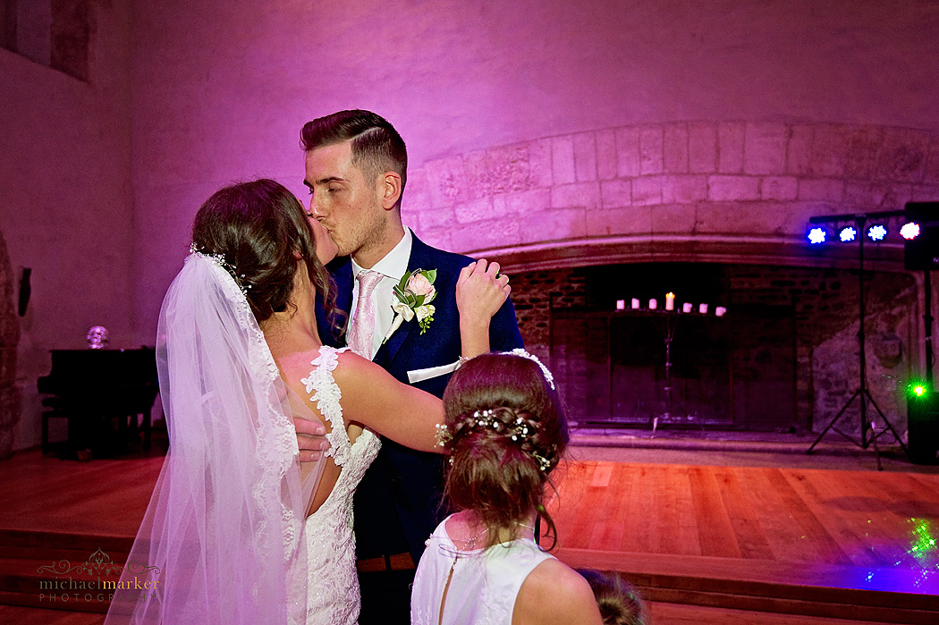 Bridesmaid looks on as bride and grooom kiss during first dance at Dartington Hall