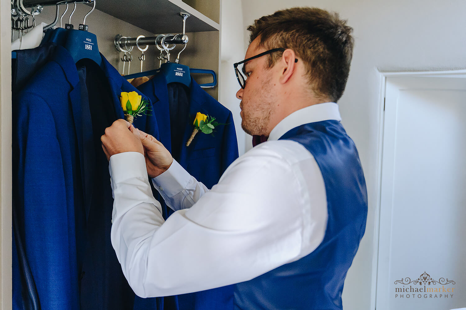 Groom attaching hand tied yellow rose button hole to his jacket at Trevenna